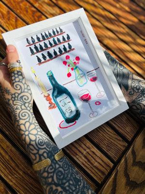 Framed artwork of bottles and glasses on a wooden surface
